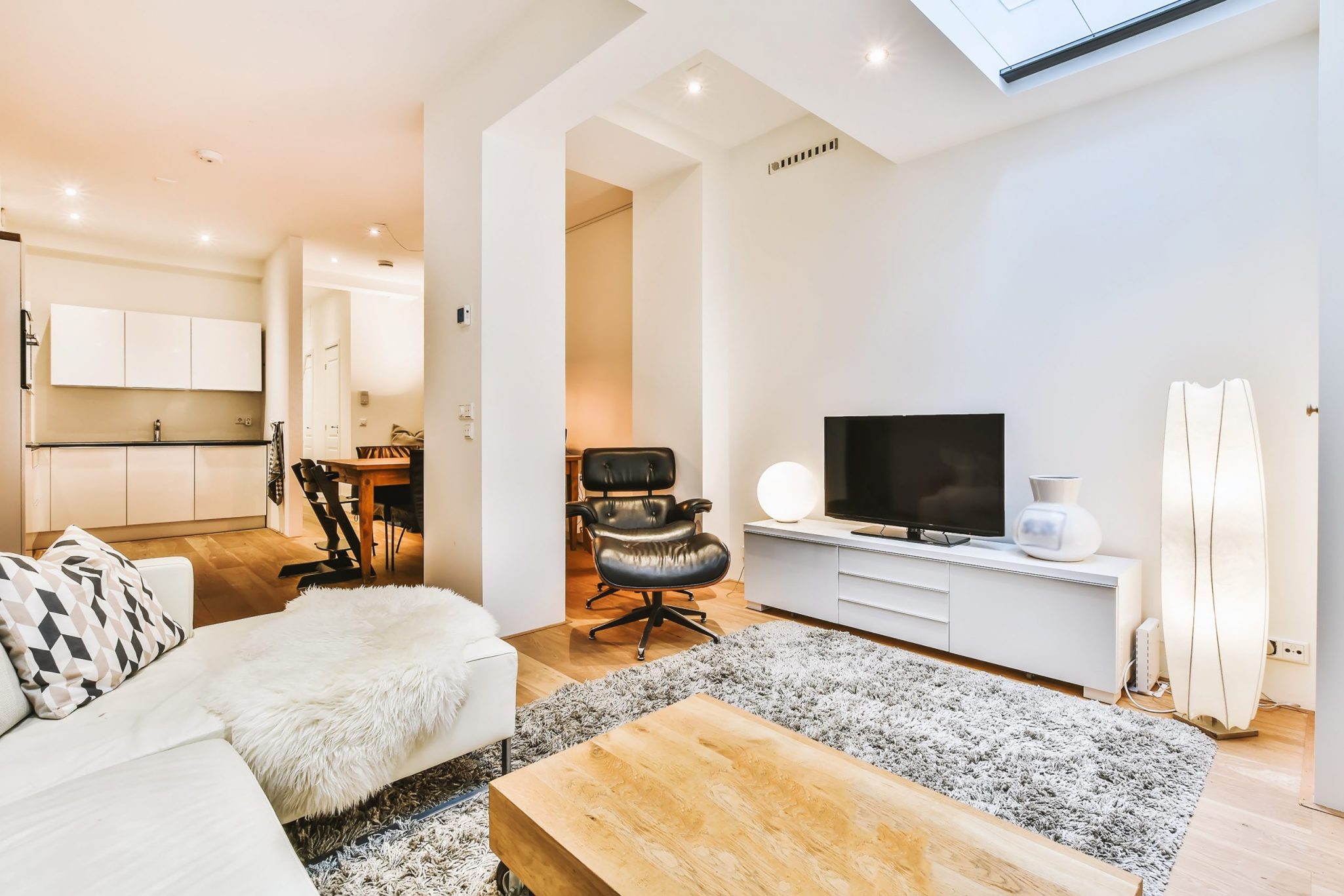 Stylish interior design of living room with light furniture and soft comfy couch and carpet and with TV on cabinet in modern apartment with open kitchen and white walls and column